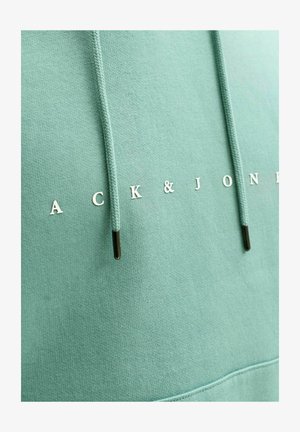 Mėtų žaliai džemperis, pagamintas iš minkštos medžiagos, su baltais užrašais "ACK & JONES" ir juodais akcentiniais elementais ant virvutės.