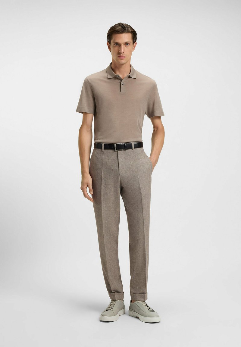 Beige polo shirt with a collar, paired with light brown patterned trousers and white sneakers. Black belt with a metal buckle.