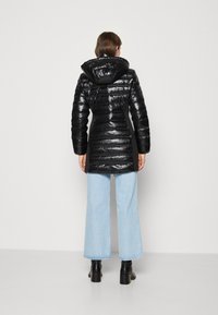 Sort dunjakke med en skinnende finish, der har en hætte og et vandret quiltet design. Sammen med lyseblå jeans med vide ben og sorte støvler.