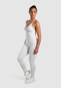 White athletic outfit featuring a fitted tank top with a gathered detail and matching leggings, both made from a smooth, stretchy fabric.