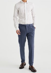 White button-up shirt and navy checkered trousers made from fabric with smooth texture. Brown loafers complement the outfit.