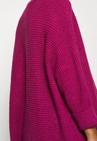Pull surdimensionné texturé en fuchsia vibrant, avec une coupe ample, des poignets côtelés et un motif tissé. Tissu doux avec une apparence douillette.