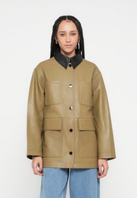 Kaki krāsas ādas jaka ar melnu apkakli, divām krūšu kabatām un centrālu melnu pogu rindu. Gluda tekstūra un vaļīgs siluets.