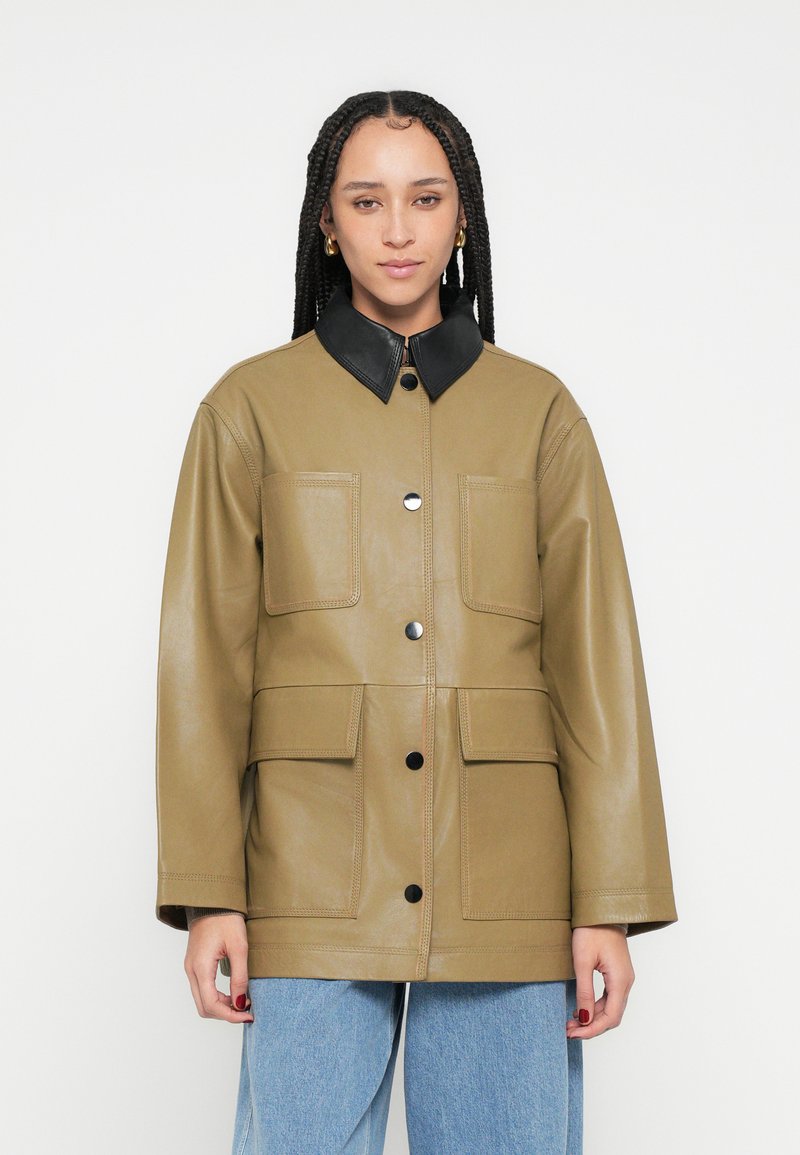 Kaki krāsas ādas jaka ar melnu apkakli, divām krūšu kabatām un centrālu melnu pogu rindu. Gluda tekstūra un vaļīgs siluets.