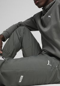Ciemnozielony dres z zamkiem błyskawicznym przy kołnierzu i elastycznymi mankietami. Biały logo Puma na klatce piersiowej i spodniach, charakteryzujący się gładką fakturą.