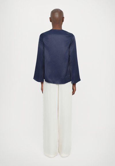 Blusa de satén azul marino con mangas largas tipo campana, escote en la espalda, combinada con pantalones de pierna ancha blancos, tejido suave y corte relajado.