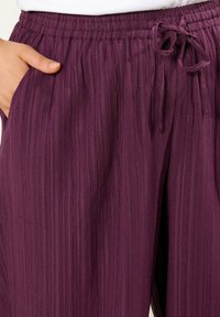 Fioletowe, marszczone spodnie z tkaniny z elastycznym paskiem w talii, regulowanym sznurkiem oraz bocznymi kieszeniami, podkreślające fakturowaną powierzchnię.