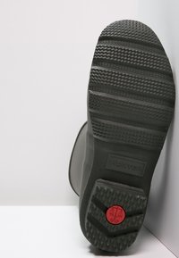 Gummistiefelsohle mit einer strukturierten schwarzen Oberfläche und Rillen für besseren Halt. Besitzt ein auffälliges rotes kreisförmiges Akzent mit Branding-Detail.