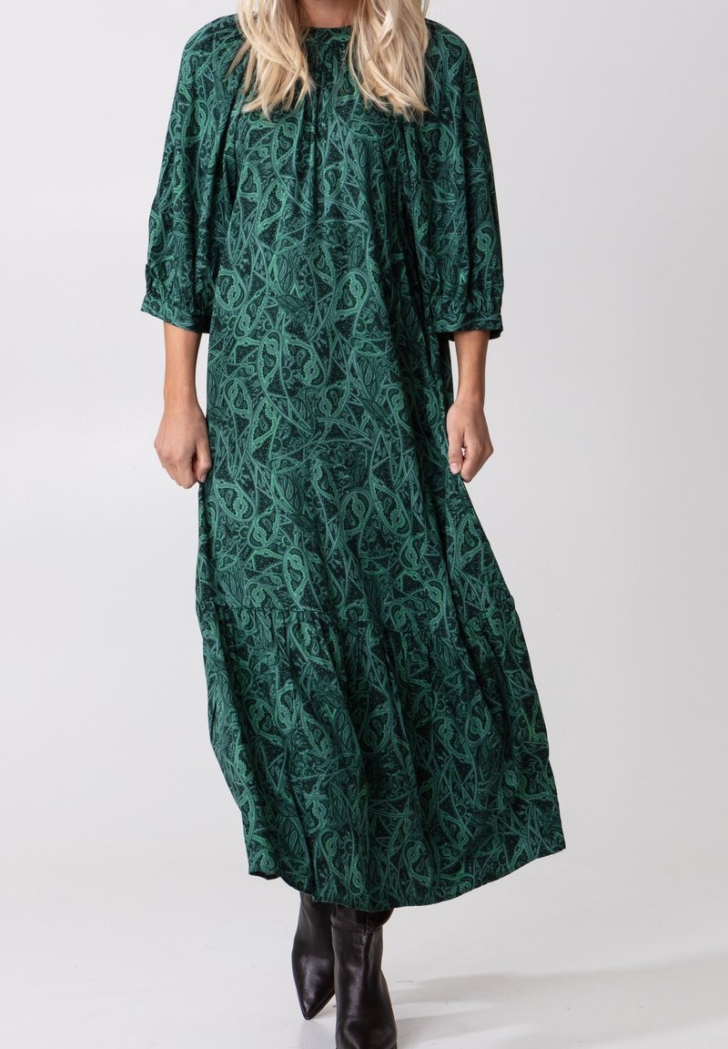 Largo vestido verde con un patrón floral, con mangas de tres cuartos y un dobladillo en capas. Hecho de tela suave, tiene un corte holgado.