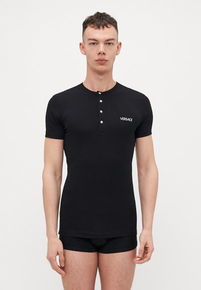 Fekete, testhez simuló, rövid ujjú henley póló, öt gombbal és fehér "Versace" logóval a bal mellrészen. Az anyaga simának és rugalmasnak tűnik.