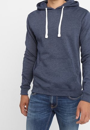 Sudadera de color azul marino en tejido suave, con mangas largas, cordones blancos, bolsillo frontal y dobladillo acanalado. Llevada con jeans azules.
