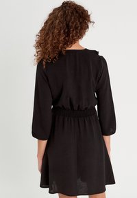 Robe noire avec des manches trois-quarts, une taille smockée et une jupe évasée. Tissu doux et léger avec une texture lisse.