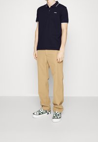 Polo shirt bleu marine à manches courtes avec des bordures blanches, pantalon kaki et baskets vertes à motifs, avec des accents graphiques et un design de col plat.