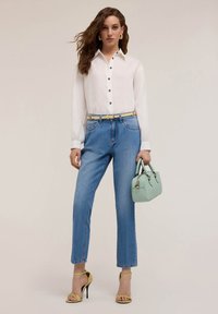 Witte overhemd met lange mouwen, blauwe jeans, gele haksandalen en een mintgroene handtas. Vlakke ondergrond, neutrale achtergrond.
