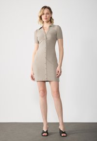 Robe à manches courtes et côtelée en beige clair avec un col, des boutons sur le devant et une silhouette ajustée. Tissu texturé.
