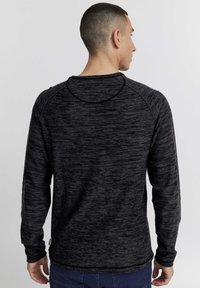Schwarzes Langarmshirt aus strukturiertem, gesprenkeltem Stoff, mit Rundhals und Raglanärmeln, gerade geschnitten am Saum.