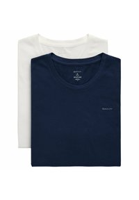 Deux t-shirts en coton de marque GANT pliés, un bleu marine devant et un blanc derrière, tous deux avec un col rond et des logos visibles.