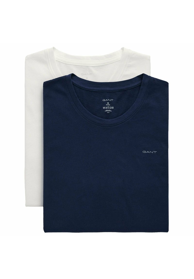 Due t-shirt di cotone del marchio GANT piegate, una blu navy davanti e una bianca dietro, entrambe con scollo rotondo e loghi visibili.