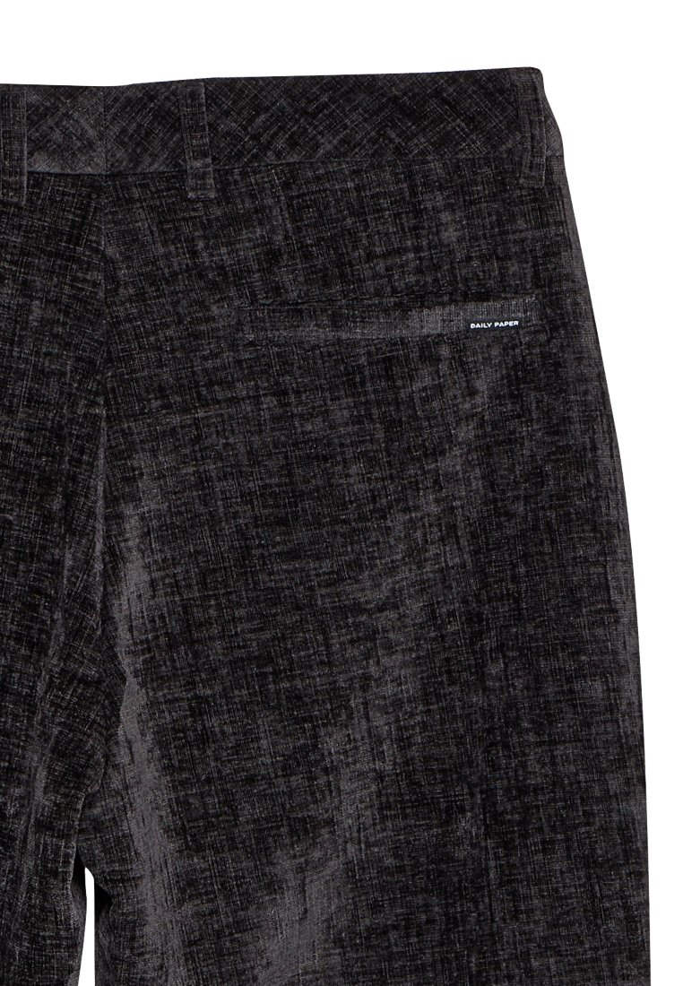 Pantalons noirs texturés avec un motif subtil, comprenant une poche arrière et une petite étiquette logo "DAILY PAPER" près de la taille.