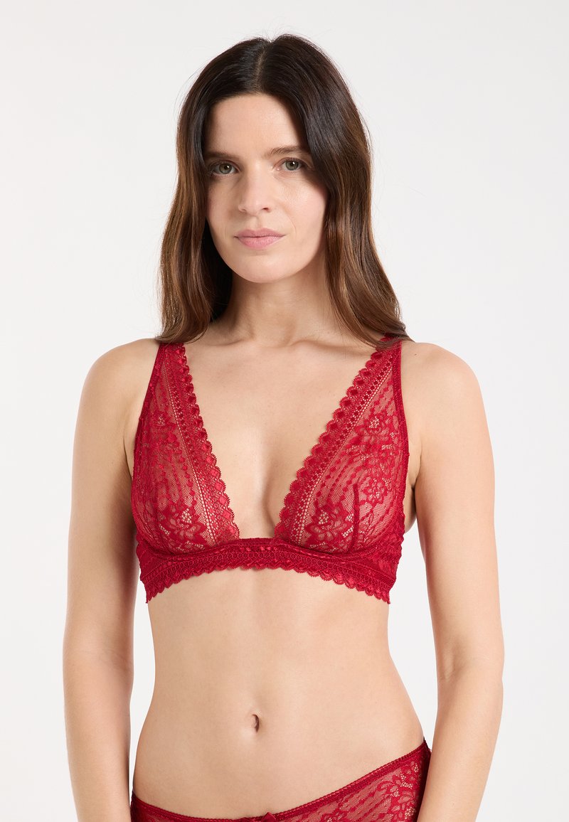 Bralette in pizzo rosso con scollo a V profondo, bordi smerlati e motivo floreale. Materiale morbido e trasparente con una finitura liscia.