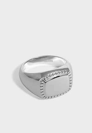 Anillo de sello de plata con una cara cuadrada lisa y líneas grabadas decorativas alrededor de los bordes sobre un fondo blanco.