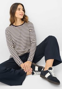 Gestreepte langste-sleeve top in crème en marineblauw, gecombineerd met marineblauwe wijde broek en zwarte suède sneakers met witte accenten en veters.