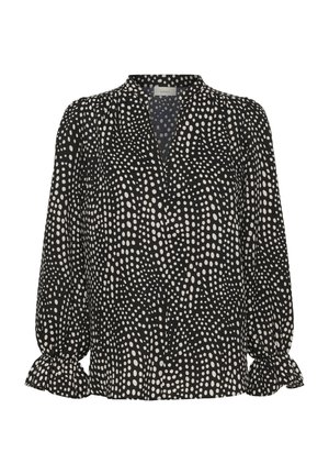 Blouse noire à pois blancs irréguliers, manches longues bouffantes avec poignets à volants, et encolure ronde avec une légère découpe en V.