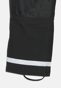 Sorte vandtætte bukser med en reflekterende hvid stribe ved kanten, holdbart stof og et fastgjort elastisk bånd til justering.
