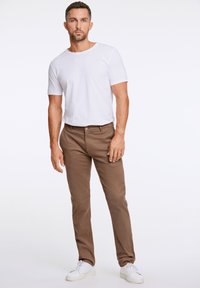 Weißes Rundhals-T-Shirt, braune Chinos und weiße Sneaker, die ein lässiges, körpernahes Design mit einer glatten Textur und einfacher Ästhetik präsentieren.