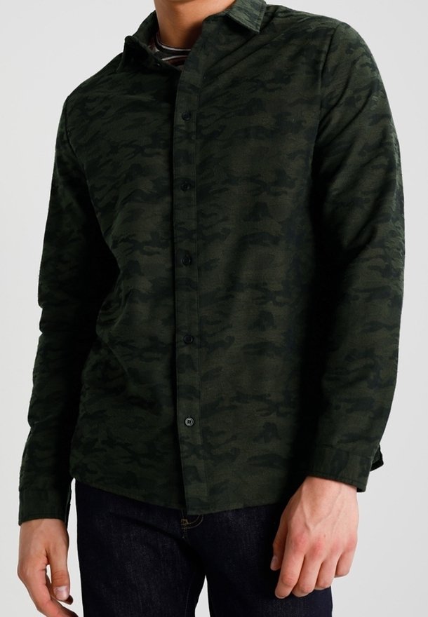 Tummanvihreä ruudullinen napillinen paita, pehmeää ja tekstuuriltaan miellyttävää kangasta. Varustettu tavanomaisella kauluksella ja napituksella. Päällä tummien farkkujen päällä.