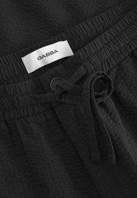 Čierne šortky z textúrovaného materiálu, s elastickým pásom, šnúrkou na stiahnutie a bielou etiketu s logom "GABBA".