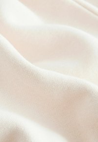 Bomuldsstof i lys beige, fint strikket med en blød tekstur, der viser bløde folder og bølger, som forbedrer dets fald og udseende.