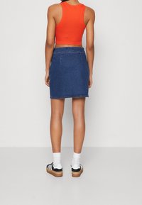 Denimminikjol med rak skärning, mörkblått tyg och vit sömnad. Kombinerad med en åtsittande röd linne och svarta sneakers.