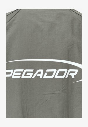 Šedé triko z látky s velkým bílým текстом "PEGADOR" a s gráfickým akcentem nad ním a jemnou texturou materiálu.
