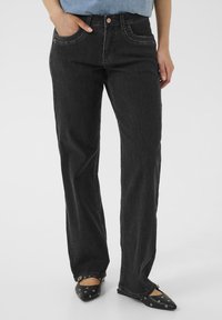 Jeans de mezclilla negra con un diseño de pierna recta, bolsillos frontales y detalles de costura visibles. Combinados con unos zapatos de punta negros.
