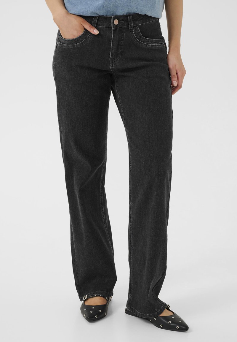 Jeans de mezclilla negra con un diseño de pierna recta, bolsillos frontales y detalles de costura visibles. Combinados con unos zapatos de punta negros.