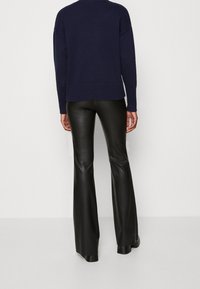 Maglione lavorato a maglia blu marina con orlo a costine, abbinato a pantaloni neri a palazzo in pelle sintetica. Tessuto morbido, vita aderente e dettagli sottili.