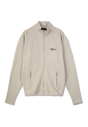 Beige ribbed zip-up jacket with stand collar, two zippered front pockets, and small black embroidered text on left chest.