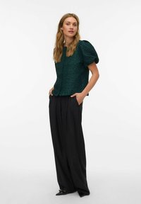 Tekstuuriga tumeroheline lühikese varrukaga pluus ümarate kaelustega, kombineeritud kõrge vöökohaga mustade laiade pükstega ja teravate mustade kingadega.