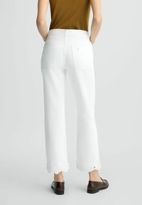 Pantalones de mezclilla blancos con un diseño de pierna recta, trimado de encaje en el dobladillo, dos bolsillos traseros y una cinturilla alta. Zapatos marrones completan el look.