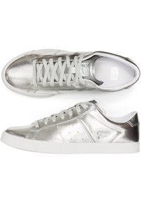 Zapatillas metálicas plateadas con una textura suave, suela de goma y lengüeta de malla. Acentuadas con perforaciones mínimas y un detalle del logo en el lado.