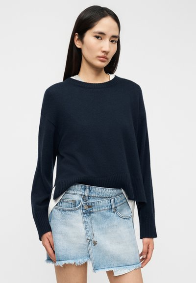 Μπλε σκούρο πλεκτό πουλόβερ με ριμπ λαιμόκοψη και τελείωμα, συνδυασμένο με ανοιχτό μπλε μίνι φούστα από τζιν με ξεφτισμένες άκρες και κλασικό σχέδιο με πέντε τσέπες.