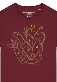 T-shirt bordeaux avec un design en ligne beige représentant des mains entrelacées avec des plantes et des fleurs, accentué de formes jaunes. Texture de tissu douce.