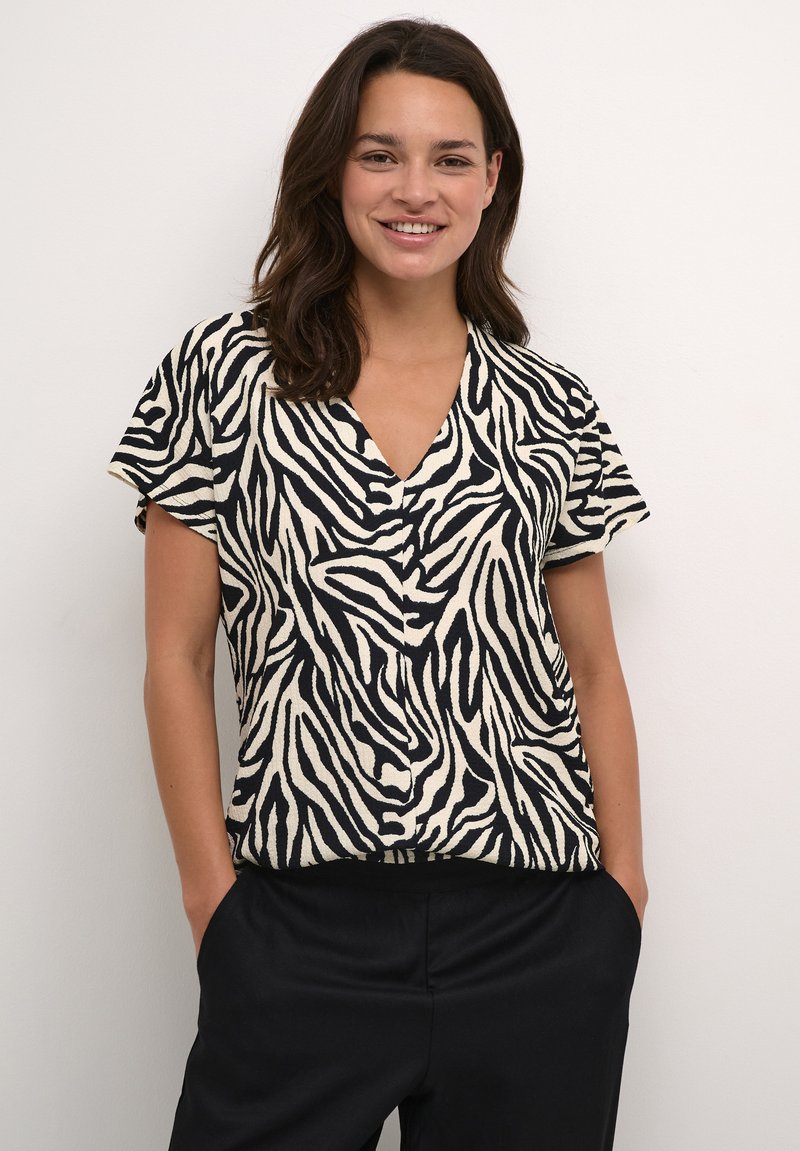 Short-sleeve top featuring a black-and-white zebra pattern; V-neck design, relaxed fit, with a textured fabric. Paired with black pants.