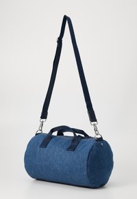 Sac cylindrique bleu en tissu texturé. Dispose de poignées en tissu doubles, d'une sangle ajustable et d'accents en métal argenté.