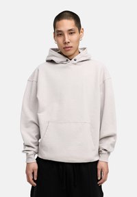 Light gray oversized hoodie made of soft fabric, featuring a front pocket, adjustable drawstring hood, and ribbed cuffs with visible stitching.