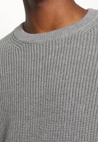 Maglione grigio lavorato a maglia con una texture a coste e un collo rotondo. Il tessuto sembra morbido e presenta un motivo uniforme in tutto il capo.