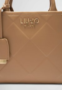 Bolso de mano acolchado en color beis, hecho de material sintético, con logotipo y herrajes en tono dorado, asas cortas y detalles texturizados.
