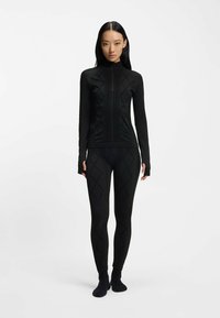 Czarna bluzka z długim rękawem i legginsy z teksturowanym geometrycznym wzorem, wykonane z elastycznego materiału dla dopasowanego wyglądu. Wysoki kołnierz i otwory na kciuki.