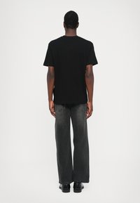 Tricou negru din bumbac cu mâneci scurte, vedere din spate, asociat cu blugi gri închis, largi și pantofi negri. Design simplu, croit.